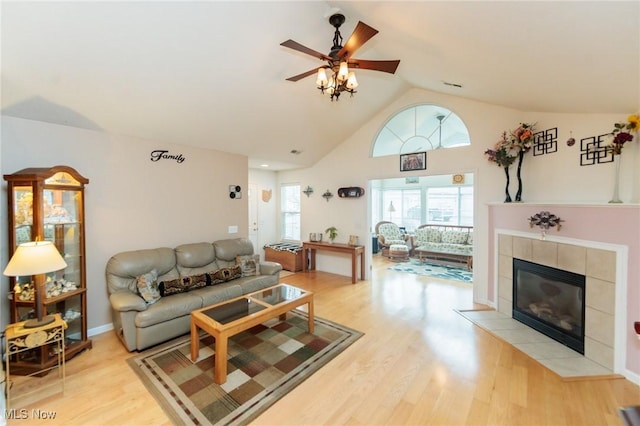 living room featuring lofted ceiling, light wood finished floors, a ceiling fan, and a tiled fireplace