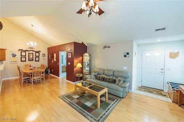 living area featuring light wood finished floors, baseboards, visible vents, lofted ceiling, and ceiling fan with notable chandelier