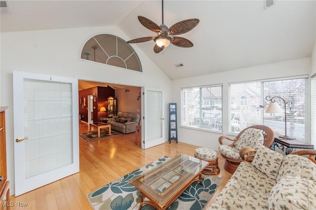 living area featuring high vaulted ceiling, light wood-type flooring, visible vents, and a ceiling fan