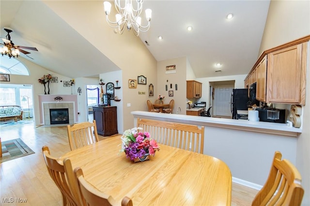 dining room with vaulted ceiling, a fireplace, light wood finished floors, and ceiling fan