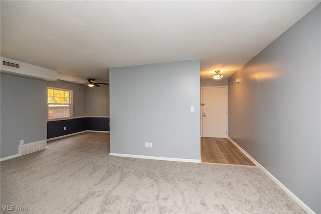 carpeted empty room with a textured ceiling, a ceiling fan, visible vents, and baseboards