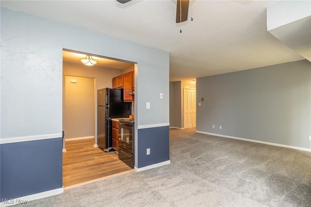 kitchen with ceiling fan, light colored carpet, baseboards, black appliances, and brown cabinetry