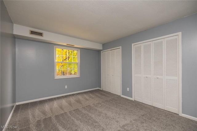 unfurnished bedroom featuring a textured ceiling, carpet flooring, visible vents, baseboards, and multiple closets