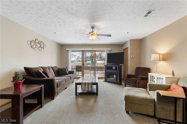 carpeted living area with a glass covered fireplace, visible vents, ceiling fan, and a textured ceiling