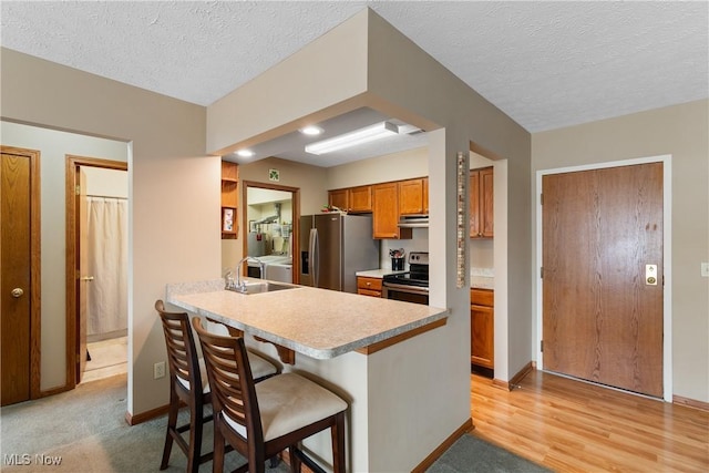 kitchen featuring brown cabinets, a breakfast bar area, washing machine and clothes dryer, appliances with stainless steel finishes, and under cabinet range hood