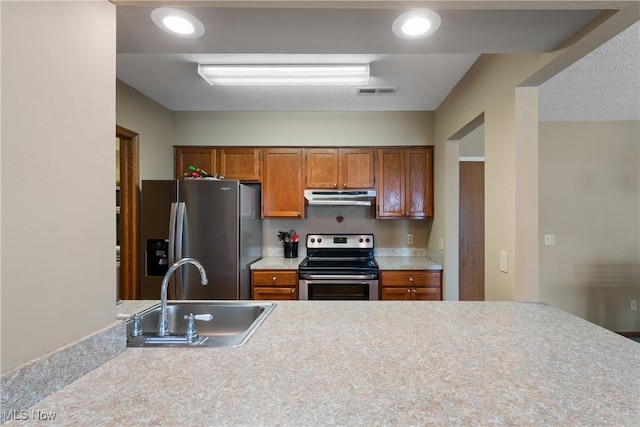 kitchen with stainless steel appliances, light countertops, brown cabinetry, a sink, and under cabinet range hood