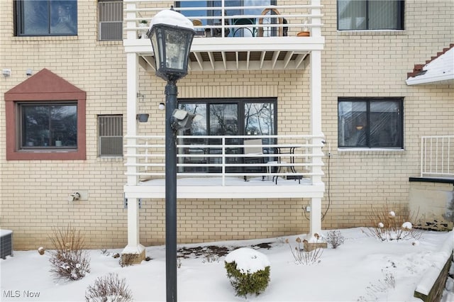 snow covered property entrance featuring a balcony and brick siding