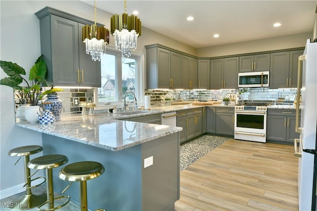 kitchen featuring light wood finished floors, stainless steel microwave, freestanding refrigerator, a peninsula, and gas stove