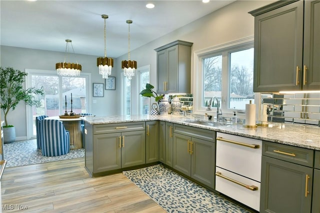 kitchen with light stone counters, a peninsula, a sink, light wood-style floors, and decorative backsplash