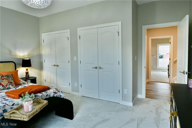 bedroom featuring multiple closets, light colored carpet, and baseboards