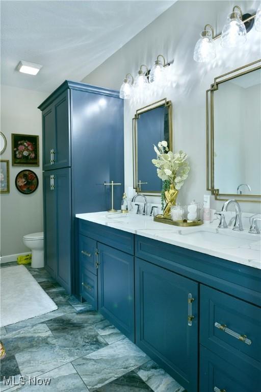 bathroom with double vanity, toilet, and a sink