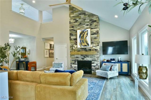 living area featuring a fireplace, ceiling fan, wood finished floors, high vaulted ceiling, and baseboards