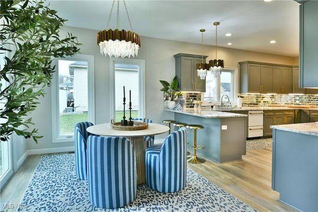 kitchen with decorative backsplash, a peninsula, light wood-style floors, pendant lighting, and a notable chandelier