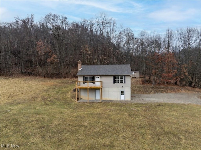 view of front of property featuring a forest view, a deck, a chimney, and a front lawn