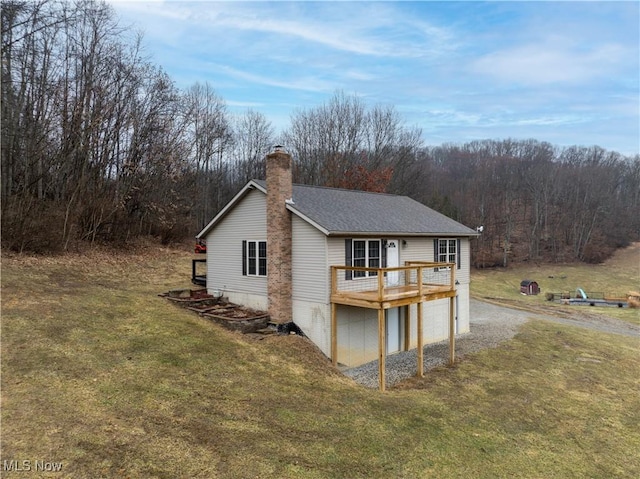 view of side of property featuring driveway, a lawn, a chimney, an attached garage, and a wooden deck