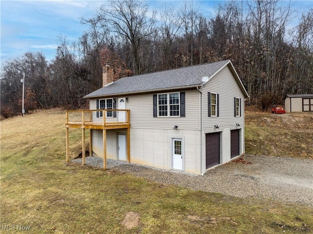 back of house featuring an outbuilding, a chimney, a lawn, a deck, and driveway