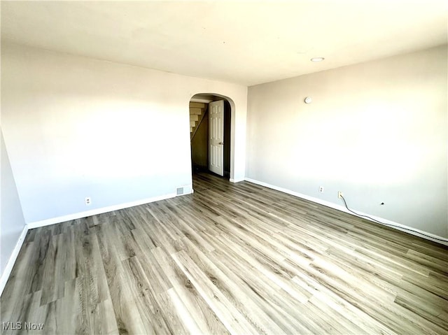 spare room with arched walkways, visible vents, baseboards, and wood finished floors