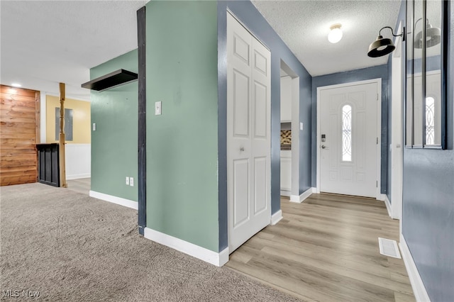 entryway featuring light colored carpet, visible vents, a textured ceiling, and baseboards