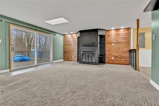 unfurnished living room with a skylight, a large fireplace, carpet flooring, wood walls, and electric panel