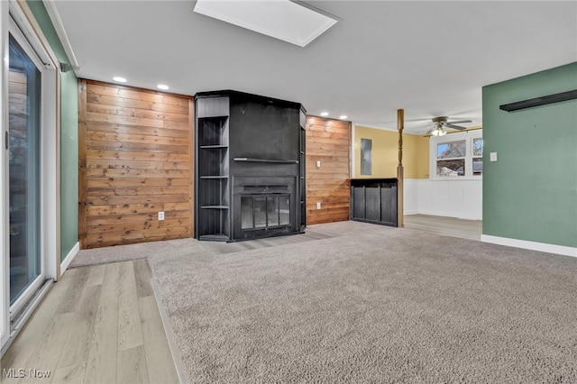 unfurnished living room with a skylight, wooden walls, a fireplace, and recessed lighting