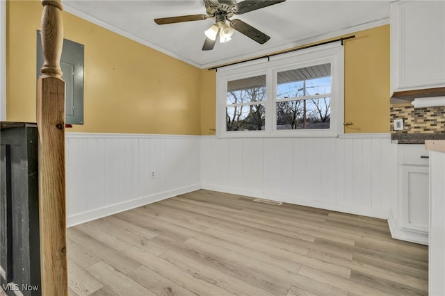 unfurnished dining area with visible vents, a ceiling fan, ornamental molding, wainscoting, and light wood-type flooring