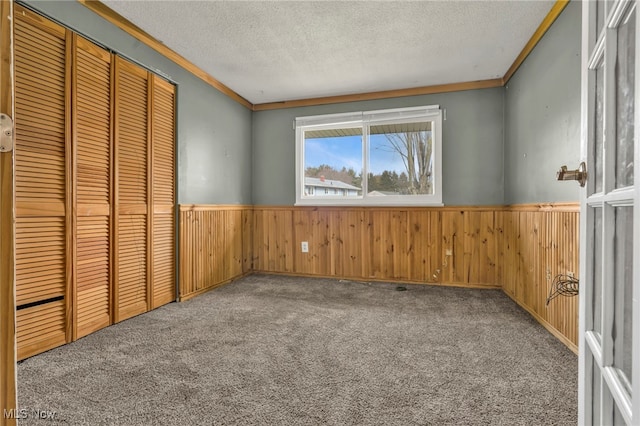 unfurnished bedroom featuring a wainscoted wall, carpet floors, and a textured ceiling