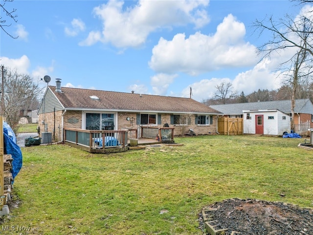 rear view of property featuring a wooden deck, fence, a yard, an outdoor structure, and brick siding