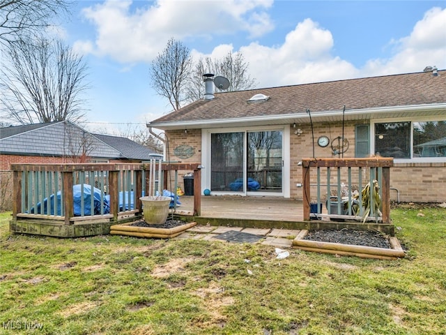 rear view of property with roof with shingles, a deck, a lawn, and brick siding