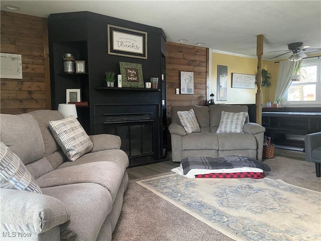 living area featuring wooden walls, ceiling fan, and a fireplace