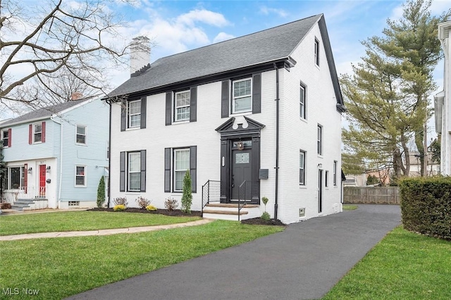 view of front of house with a front yard, brick siding, fence, and a chimney