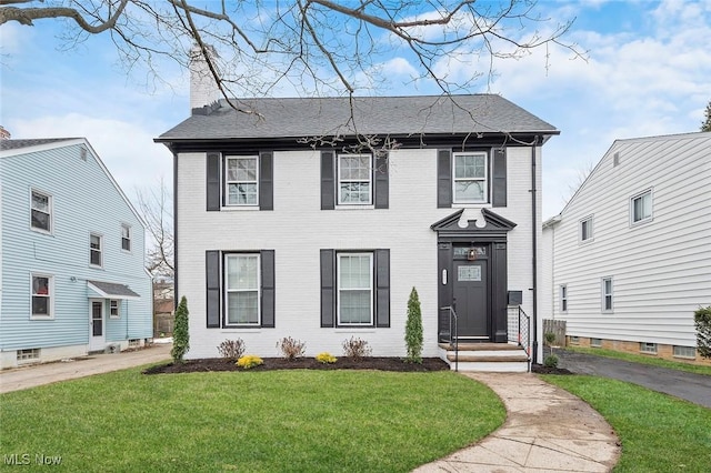 colonial inspired home with brick siding, a chimney, and a front lawn