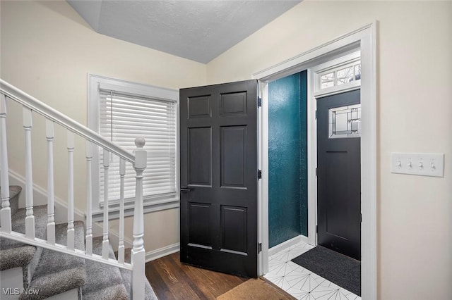 entrance foyer with lofted ceiling, stairway, a textured ceiling, wood finished floors, and baseboards