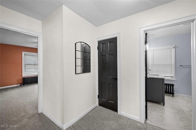 hall featuring radiator heating unit, baseboards, and light colored carpet