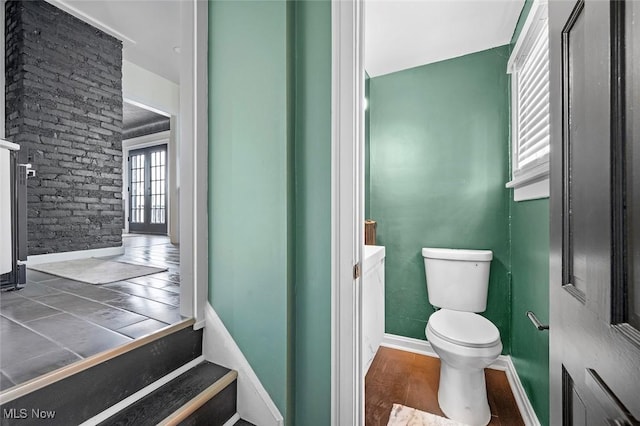 bathroom featuring brick wall, baseboards, toilet, and wood finished floors