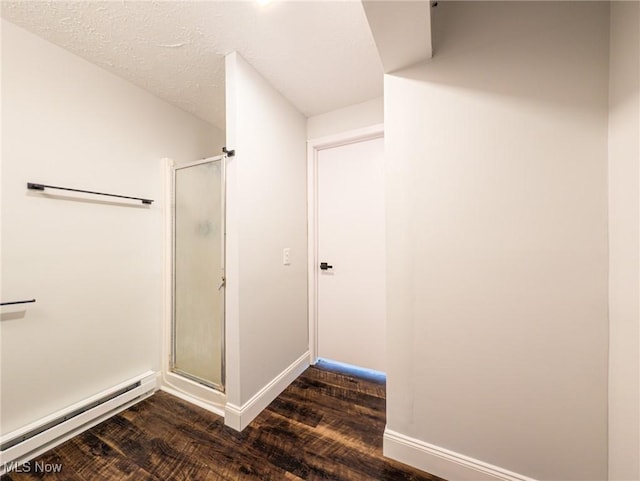 bathroom with a baseboard radiator, a textured ceiling, a shower stall, wood finished floors, and baseboards