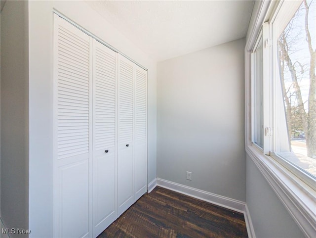 unfurnished bedroom featuring dark wood-style flooring, a closet, and baseboards