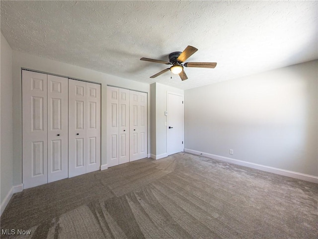 unfurnished bedroom featuring carpet floors, a textured ceiling, baseboards, and two closets