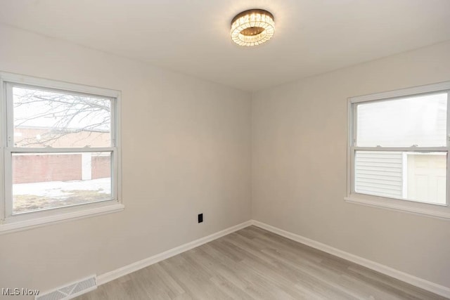 spare room featuring light wood finished floors, visible vents, and baseboards