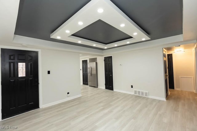 empty room featuring light wood-style flooring, visible vents, a raised ceiling, and baseboards