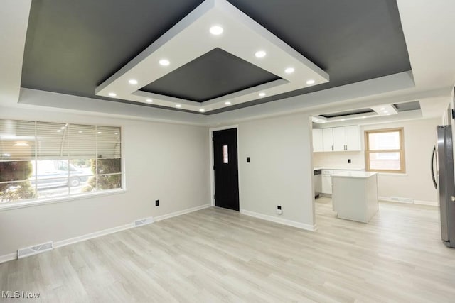 unfurnished living room featuring light wood-style floors, a raised ceiling, visible vents, and baseboards