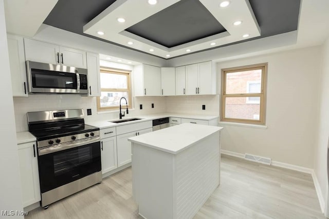 kitchen featuring stainless steel appliances, a sink, visible vents, decorative backsplash, and a raised ceiling