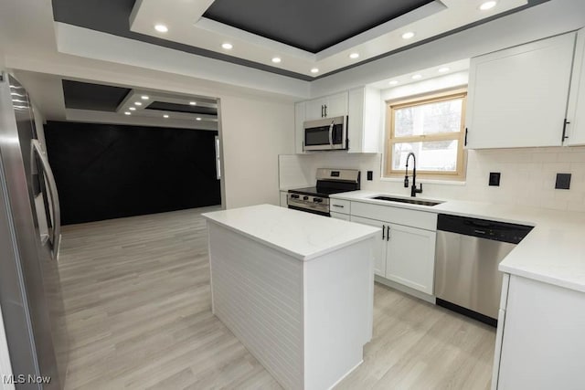 kitchen featuring a raised ceiling, appliances with stainless steel finishes, a center island, white cabinetry, and a sink