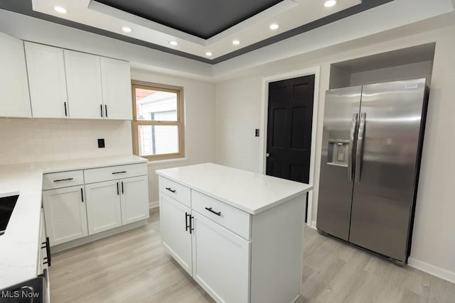 kitchen with light wood-style flooring, white cabinetry, stainless steel refrigerator with ice dispenser, and a raised ceiling