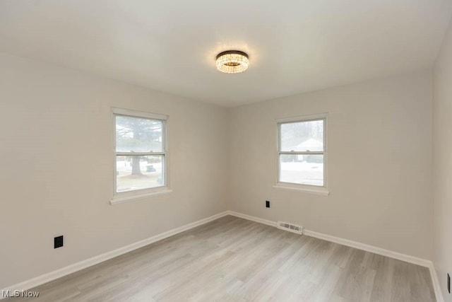 empty room with light wood-type flooring, visible vents, and a wealth of natural light