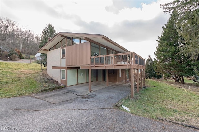 rear view of house with driveway, a carport, a lawn, and a wooden deck