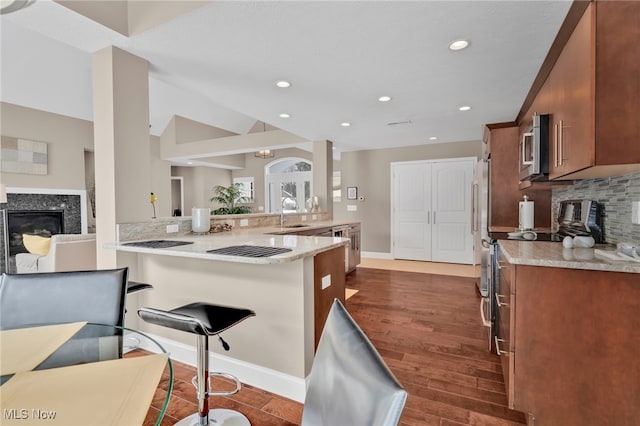 7571 Silverleaf Ct, Sagamore Hills, OH 44067 - kitchen with a premium fireplace, decorative backsplash, dark wood-type flooring, a kitchen bar, and stainless steel appliances