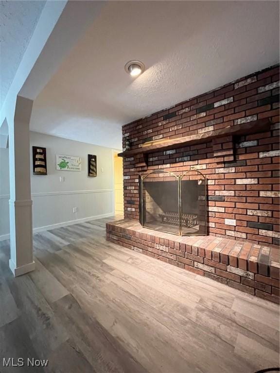 unfurnished living room featuring a brick fireplace, brick wall, baseboards, and wood finished floors