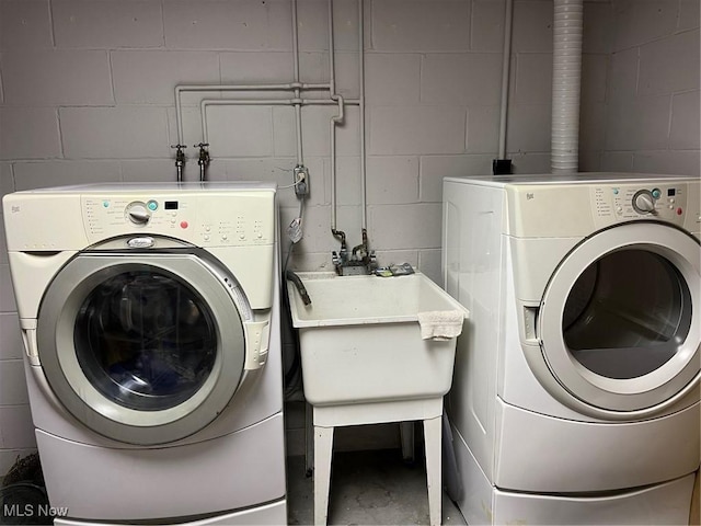 clothes washing area featuring a sink, laundry area, washing machine and clothes dryer, and concrete block wall