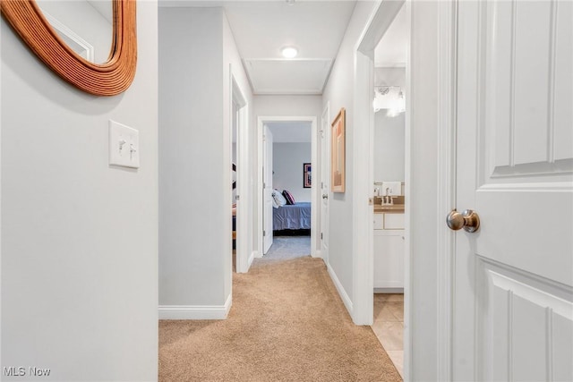 corridor with light carpet, a sink, baseboards, and light tile patterned flooring