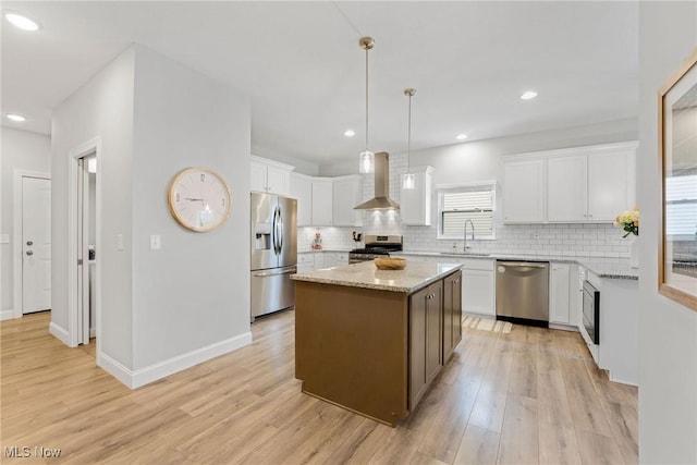 kitchen featuring a sink, appliances with stainless steel finishes, wall chimney range hood, and light wood-style floors